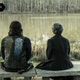 Daryl and Carol sit on a stone bench overlooking a small, placid lake.